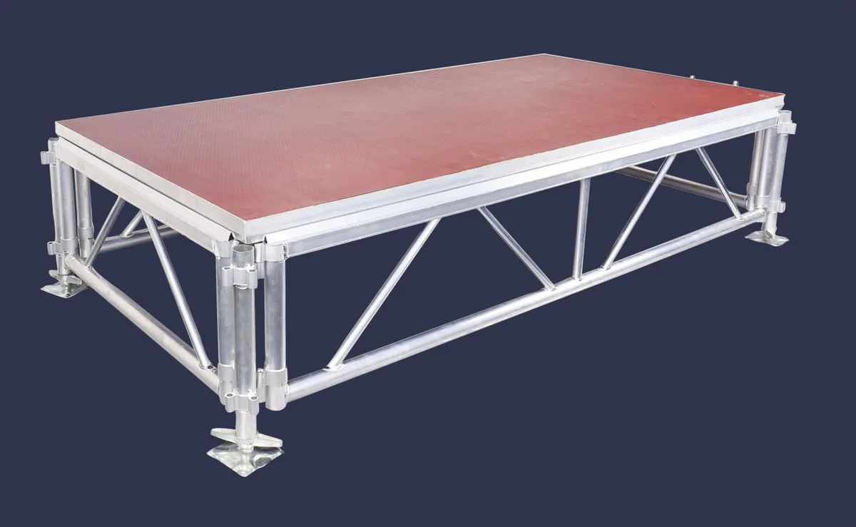 Aluminum truss-braced stage platform with a red anti-slip deck and adjustable feet